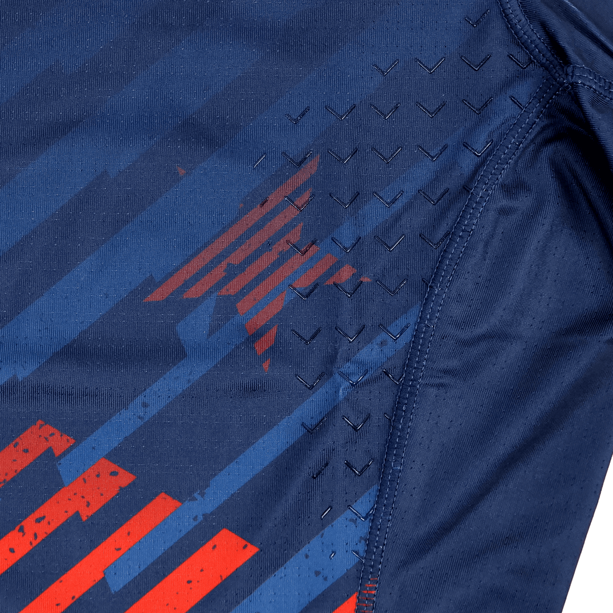 Close-up of the Castore USA Rugby 24/25 7s Olympic Pro Home Jersey’s navy athletic fabric, featuring red stripes, a subtle star pattern, and black chevron-textured grips near the seam.