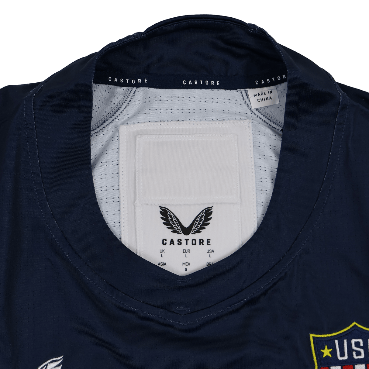 Close-up of the USA Rugby 24/25 7s Olympic Pro Home Jersey collar by Castore, showing the brand label, size tags, and "Made in China" text. A portion of the USA Rugby badge is visible on the right.