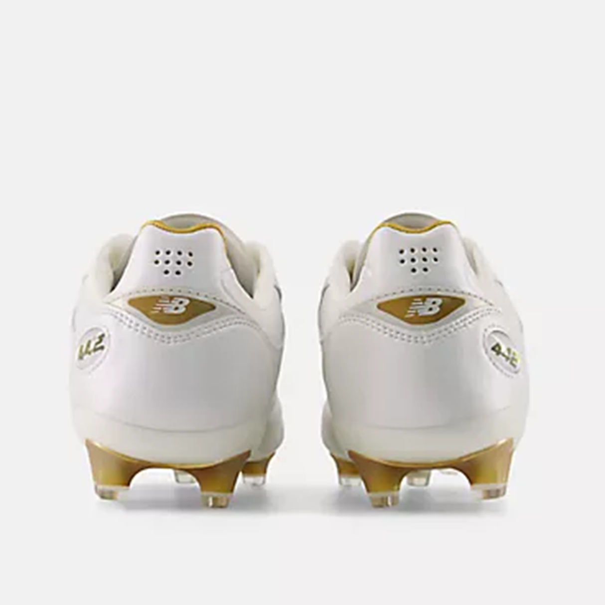 A pair of New Balance 442 Elite FG v3 soccer cleats in Sea Salt/Gold Metallic, featuring a microfiber upper, shown from the back on a plain background.