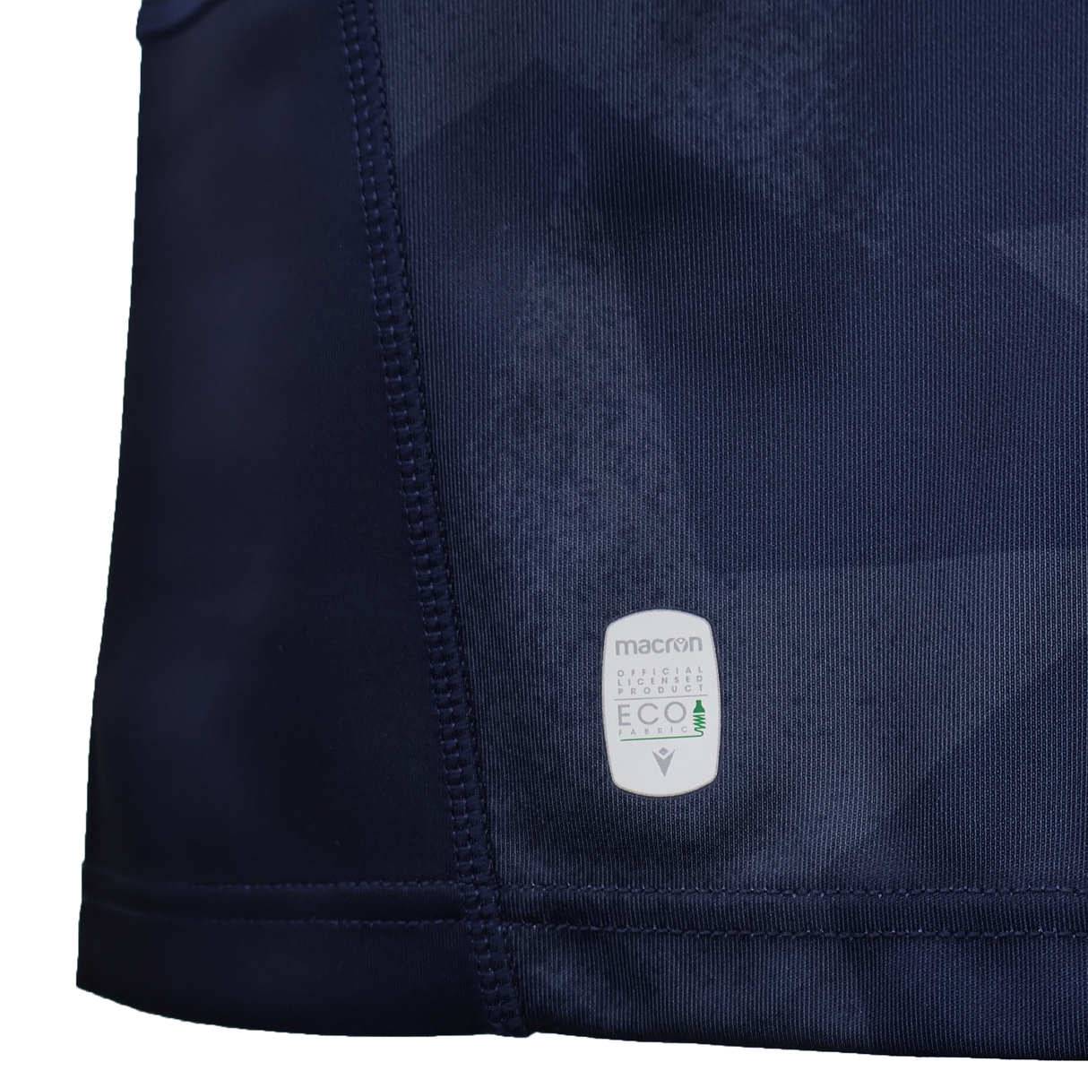 Close-up of the dark blue USA Rugby WRWC25 Replica Home Jersey by Macron, featuring a stitched seam and a white "macron ECO" tag that highlights its sustainable materials—part of the official collection for Women's Rugby World Cup 2025.