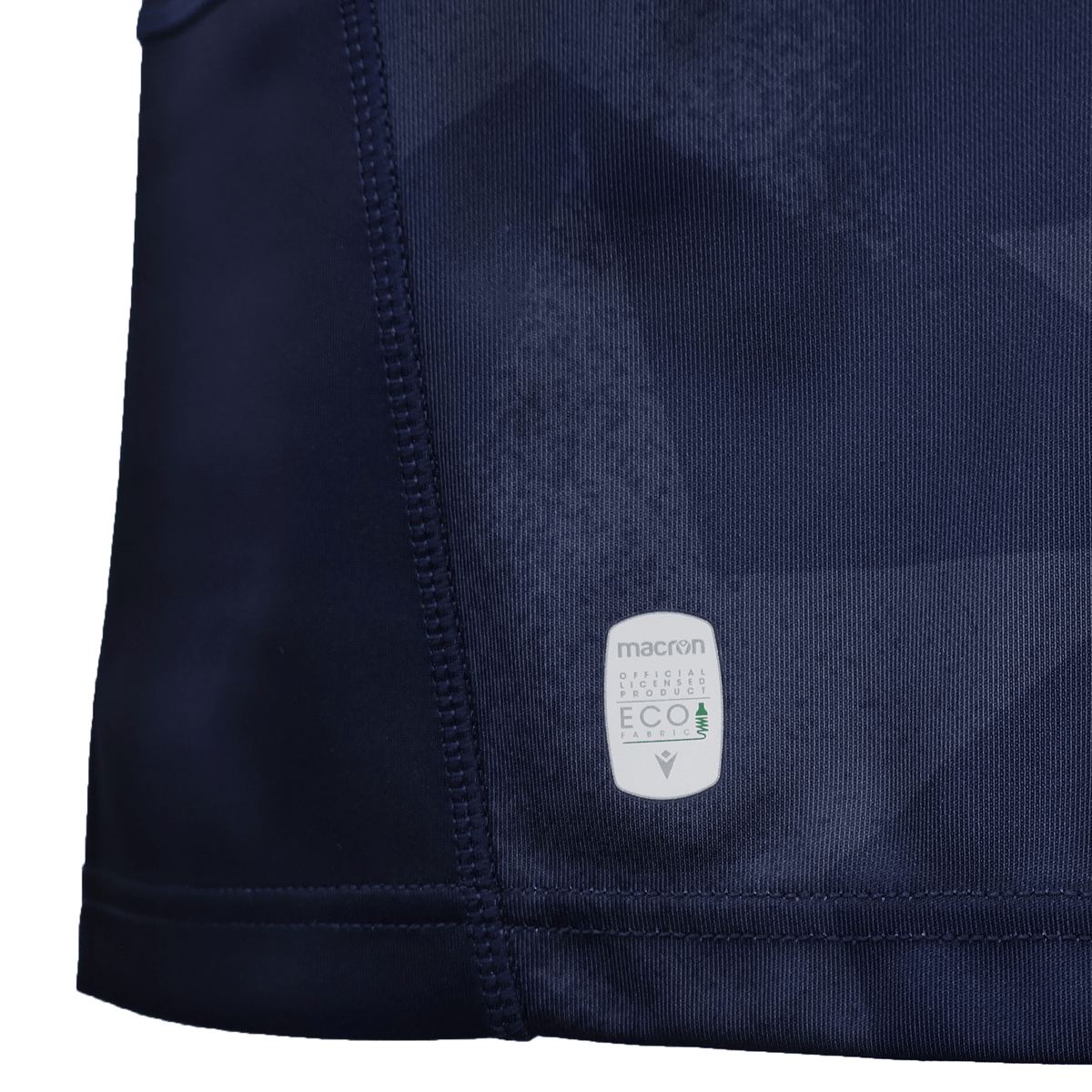 Close-up of the dark blue USA Rugby WRWC25 Replica Home Jersey by Macron, featuring a stitched seam and a white "macron ECO" tag that highlights its sustainable materials—part of the official collection for Women's Rugby World Cup 2025.