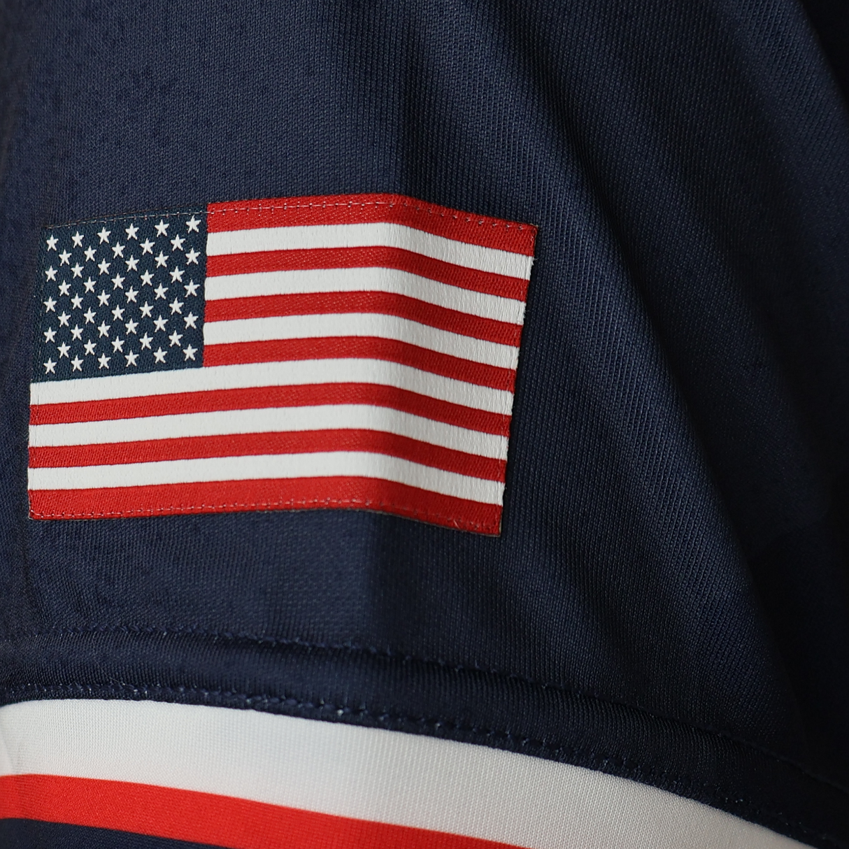 A close-up of an embroidered American flag patch on the dark blue USA Rugby WRWC25 Replica Home Jersey by Macron, designed for the Women's Rugby World Cup 2025.