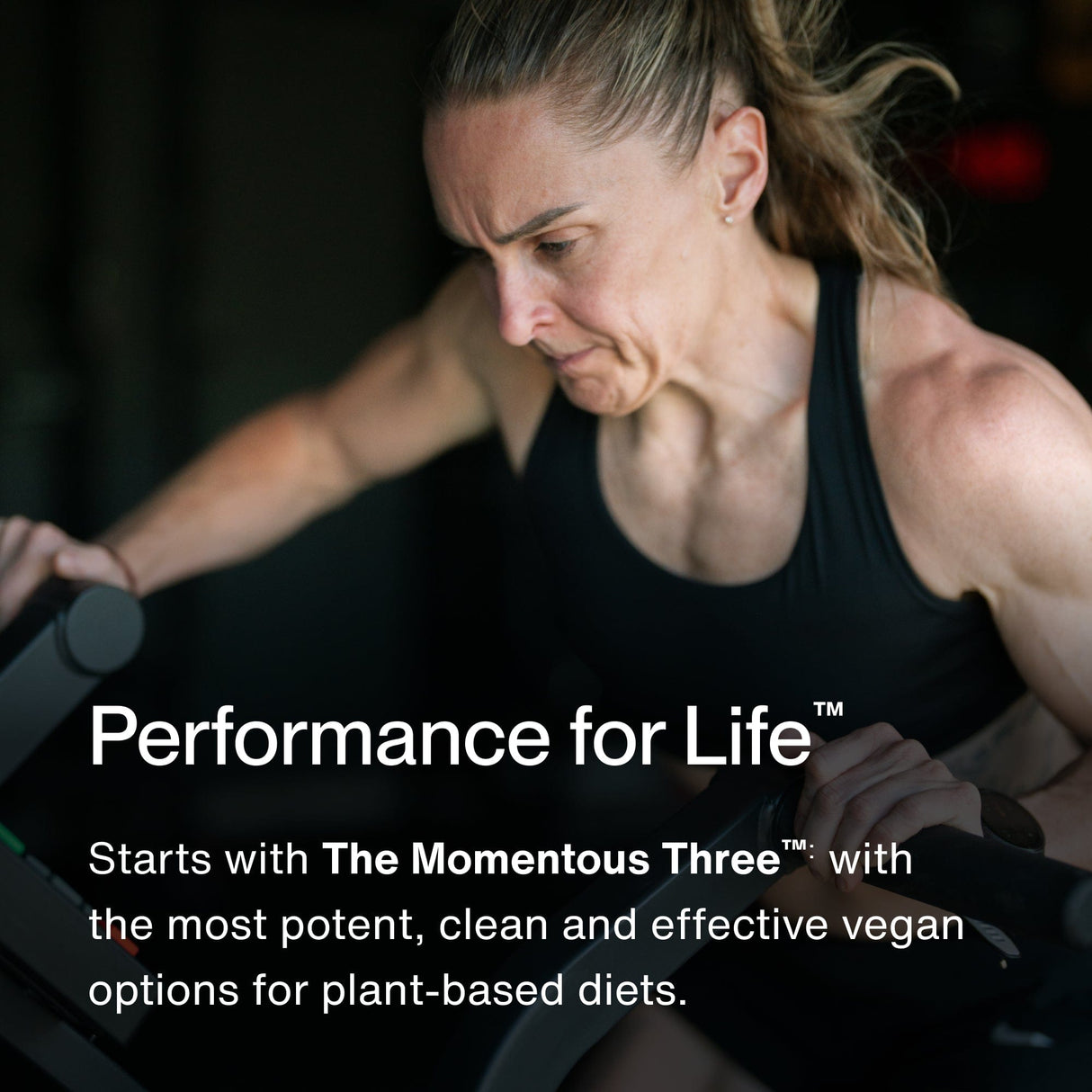 A focused woman in athletic wear exercises on a cardio machine. Text promotes Momentous The Momentous Three - Vegan supplements, supporting plant-based diets with vegan protein and omega-3s.
