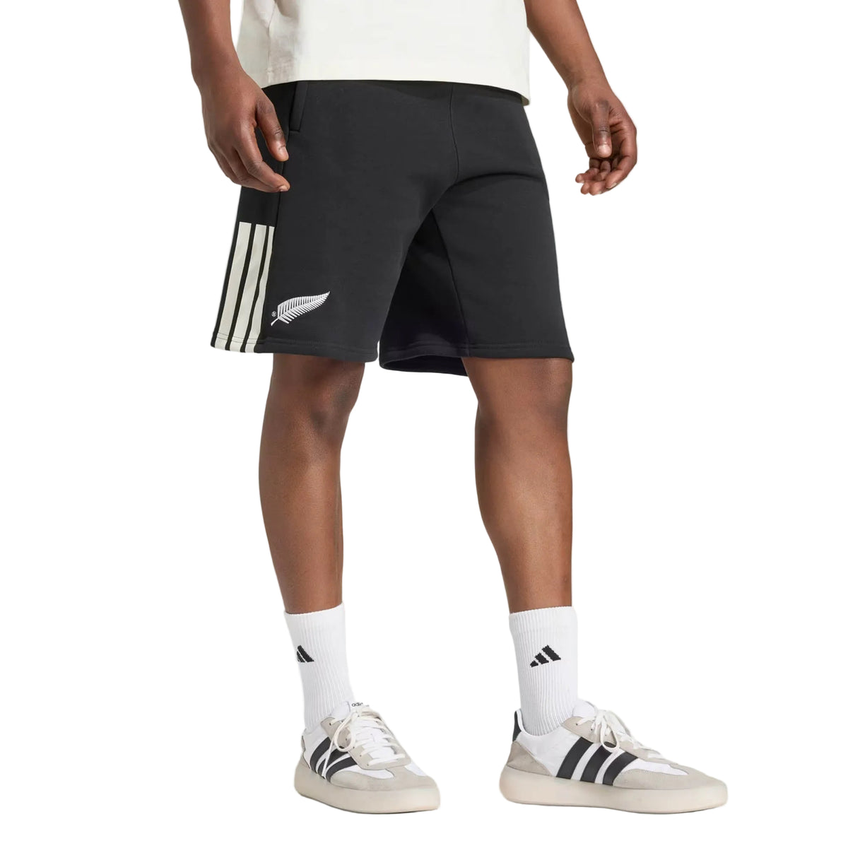 Wearing a white shirt, white crew socks, and white adidas sneakers with black stripes, this person completes their look with All Blacks 26/27 Leisurewear Shorts by adidas.