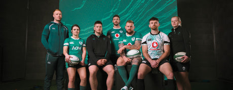 A group of seven rugby players, four men and three women, dressed in rugby uniforms, hold rugby balls and pose for a photo against a green background.