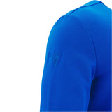 Close-up of a person wearing the Italy 25/26 Vintage Long Sleeve Supporters Jersey by Macron, a bright blue rugby-style shirt with a small embossed logo on the upper sleeve.