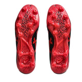 The ASICS Lethal Flash IT FF 3 FG firm ground boots in Black/Speed Red are shown from the bottom, highlighting their multiple studs and textured sole design against a white background.