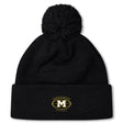 The Monarch Rugby Club Pom Pom Beanie by EMB Canterbury is a black, fleece-lined hat with a pom-pom and an embroidered gold "M" Monarch Rugby logo on the front cuff.