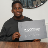 A man in a dark sweatshirt sits at a table holding an "ICONS.com SIGNED BY THE WORLD'S BEST" sign, next to an Icons Maro Itoje Signed British & Irish Lions Rugby Ball.