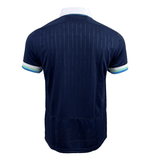 The Scotland Replica Home Jersey 24/25 by Macron is a navy blue short-sleeve sports jersey, viewed from the back, featuring a white collar and multi-colored sleeve edges. Made of 100% Polyester, this Macron home replica shirt is perfect for any fan of Scotland Rugby Union.