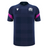 The Scotland 25/26 Player Training T-Shirt by Macron features a navy blue checkered pattern, white chest logos, and pink sleeve stripes—an ideal moisture-wicking sports tee for fans and athletes from Macron.