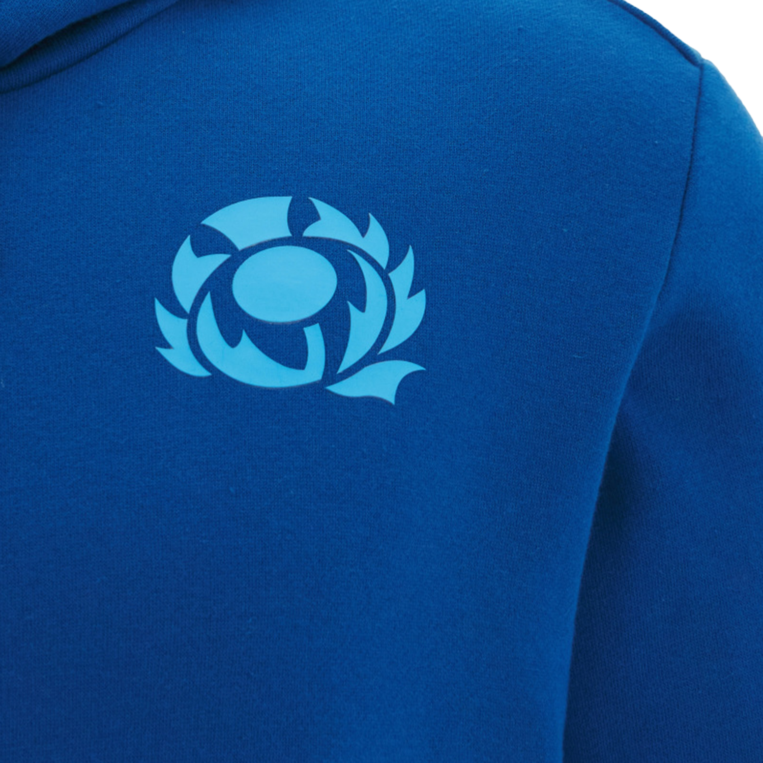 Close-up of the Scotland 25/26 Murrayfield Stadium Hoodie by Macron, a blue sweatshirt featuring a light blue circular emblem with stylized leaf shapes on the chest, echoing classic Macron Scotland style.