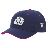 The Scotland 25/26 Baseball Cap by Macron features navy blue fabric, a white floral emblem on the front, a Scottish Rugby logo on the side, and pink accents highlighting the eyelets and brim edge.
