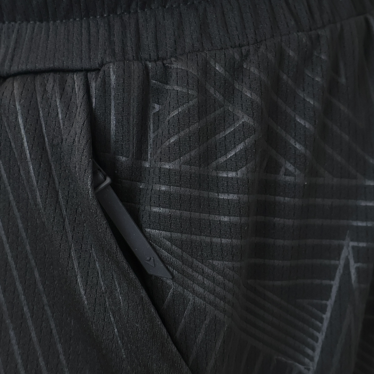 Close-up of the Wales 25/26 Basketball Shorts by Macron, featuring black textured fabric with a diagonal zipper pocket and subtle geometric line patterns, reflecting an athletic fit design typical of Macron sportswear.