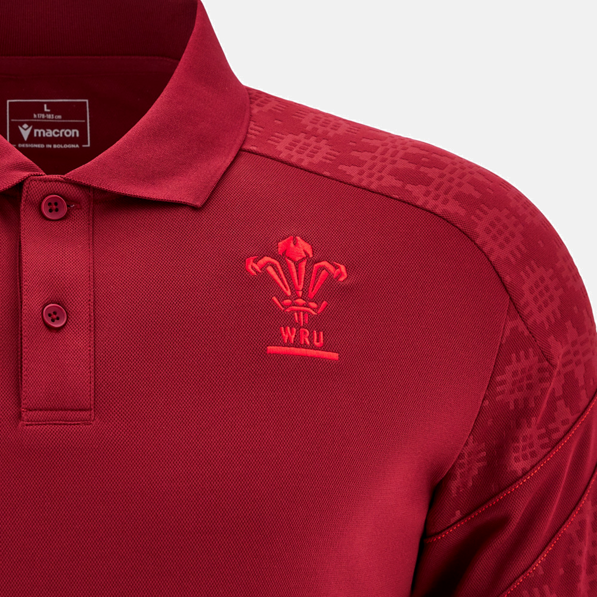 A close-up of the Wales 25/26 Player Travel Poly Polo by Macron, featuring the Welsh Rugby Union logo on the chest and patterned shoulders—a stylish classic for any fan.