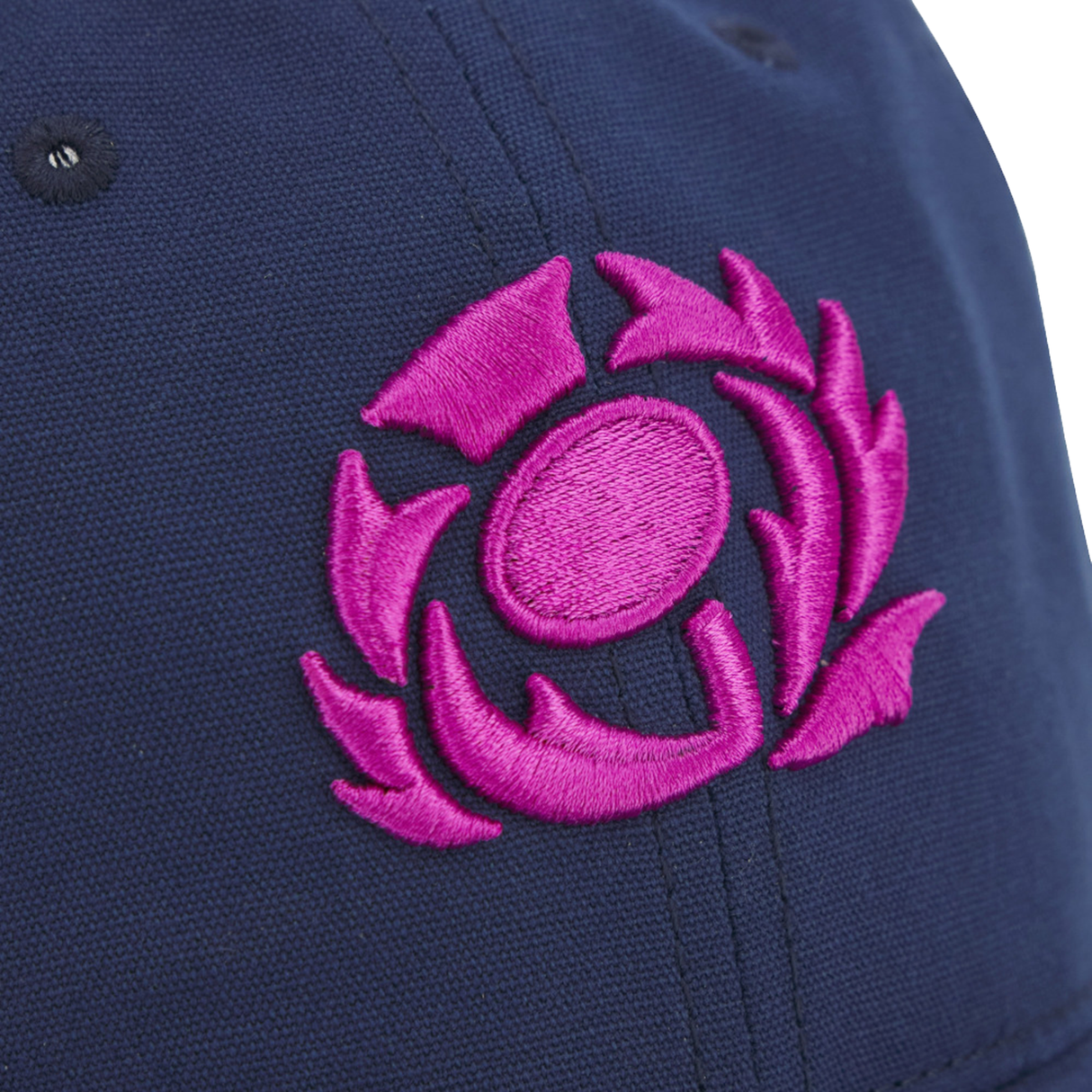 Close-up of the Scotland 25/26 Dad Cap by Macron, a navy blue hat featuring a pink embroidered abstract circular thistle-inspired design.