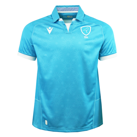 The Uruguay URU 25/26 Replica Home Jersey by Macron features light blue short sleeves, white trim, a stylized bird crest with “URU” text on the chest, and subtle sunburst patterns, all made from EcoFightex fabric.