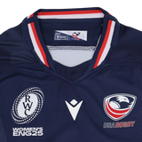 The Youth USA Rugby 24/25 Home WRWC Jersey by Macron features USA Rugby and Women's RWC England 2025 logos, red/white/blue collar detailing, and an official Macron design for comfort and style.
