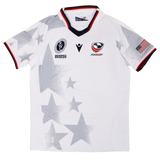 The Youth USA Rugby WRWC 25 Home Jersey by Macron features gray star patterns, the "USA Rugby" logo, WRWC 25 emblem, American flag patch, plus red, white, and blue trim on the sleeves and collar.