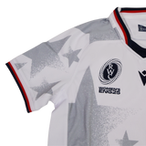 The Youth USA Rugby WRWC 25 Home Jersey by Macron features white fabric, gray star patterns, a red, white, and blue collar, and chest emblems reading “RWC,” “Women’s ENG25,” and “WRWC 25.”.