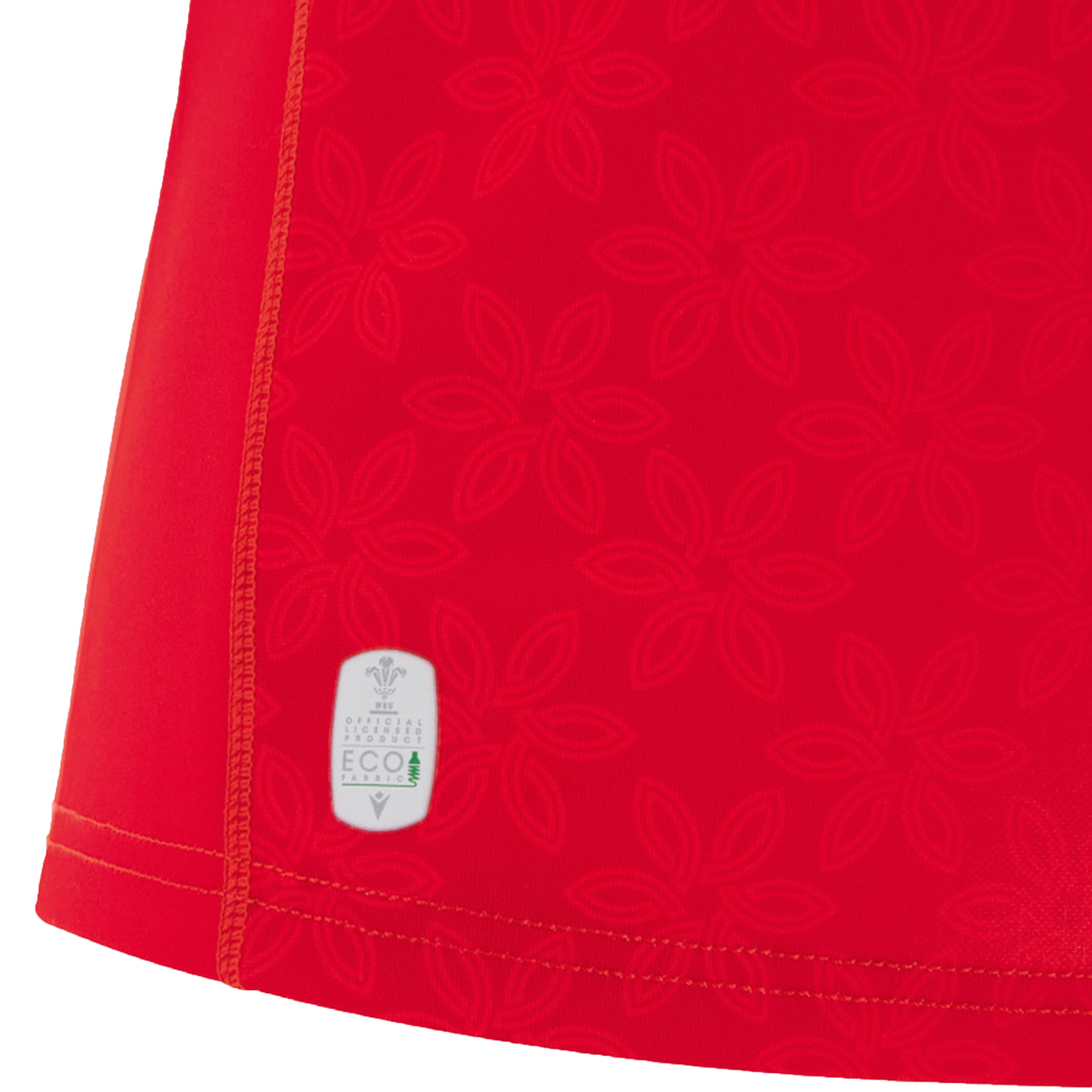 Close-up of red fabric with a subtle floral pattern and a small white eco label near the hem—part of the Women's Wales WRWC25 Replica Home Jersey by Macron.