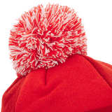 A close-up of the Wales 25/26 Pom-Pom Beanie by Macron, a red knit hat with a bold red and white pom-pom, perfect for Welsh Rugby Union fans seeking cozy winter style.