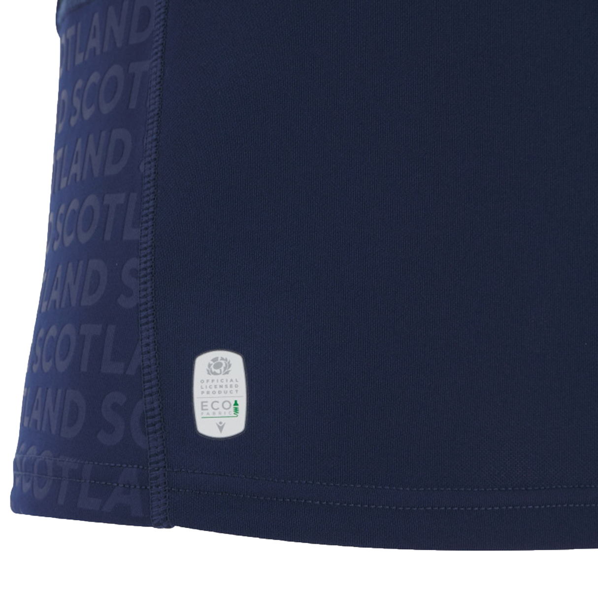 Close-up of dark blue fabric with repeated "SCOTLAND" text and an "Official Licensed Product ECO" label near the seam—part of the Women's Scotland WRWC25 Replica Home Jersey by Macron.