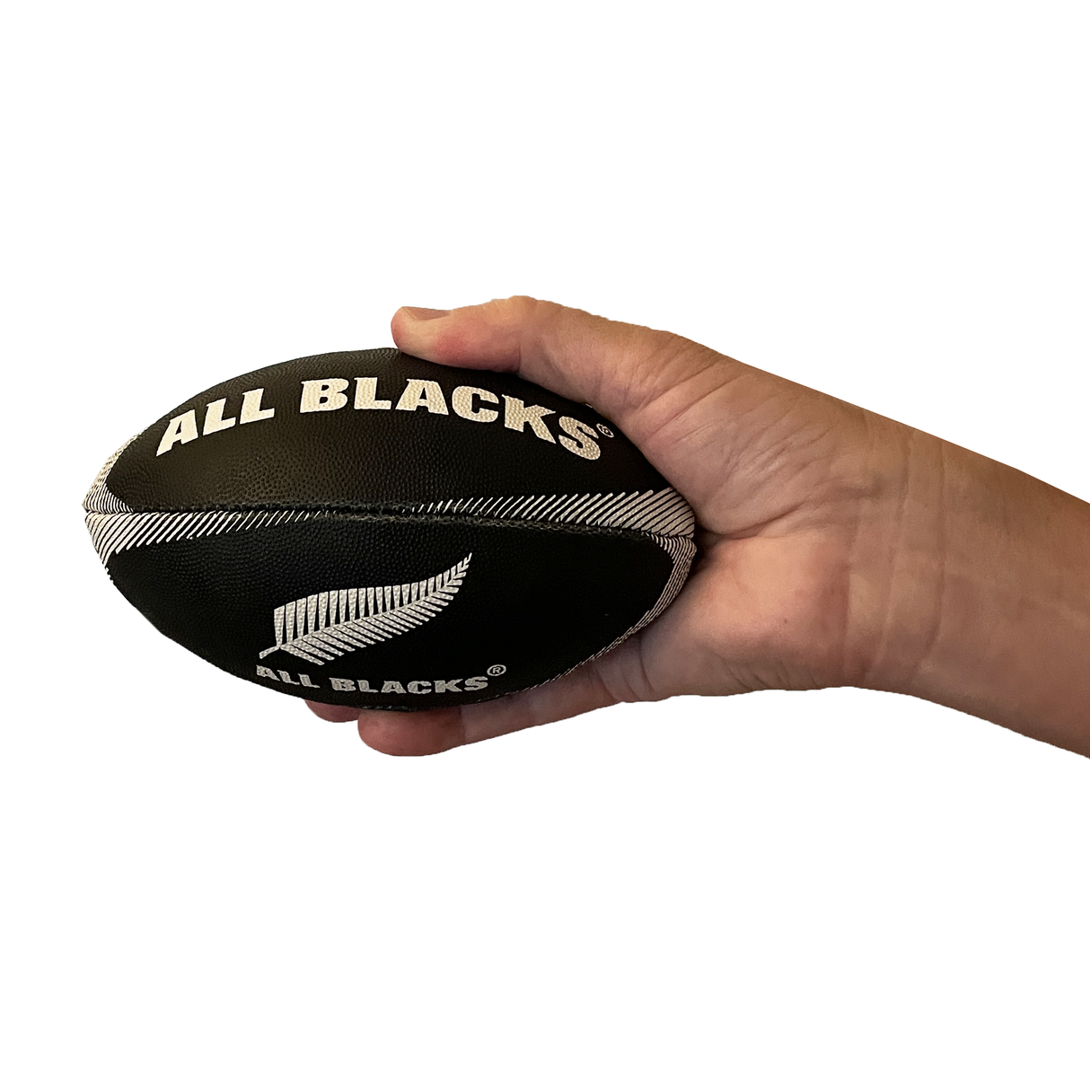 A hand holds the All Blacks Mini Supporters Ball by Gilbert, a small black rugby ball featuring "ALL BLACKS" and a silver fern logo, against a white background.