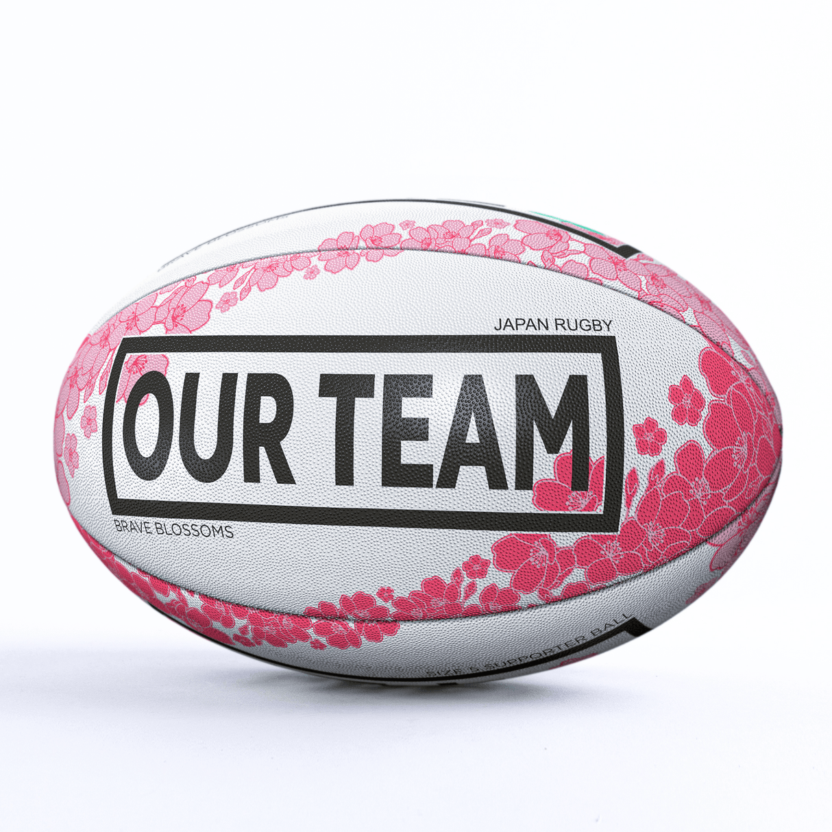 A rugby ball decorated with pink flower designs and the text "OUR TEAM," labeled "Japan Rugby" and "Brave Blossoms," this Japan Supporters Ball by Gilbert is perfect for fans cheering on their national team.