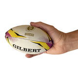 A hand holds the Gilbert Women's Rugby World Cup 2025 Official Replica Mini Ball, displaying its white, yellow, and purple design against a plain background.