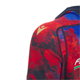 Close-up of a person's shoulder wearing the Italy 25/26 Replica Training Jersey by Macron, featuring red, blue, and black patterns with a yellow logo on the shoulder.