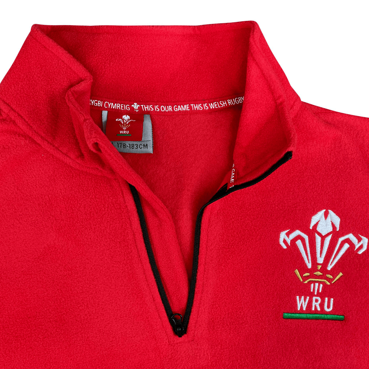 The Macron Wales Rugby Union 1/4 Zip Fleece Top is shown on a red sweatshirt.