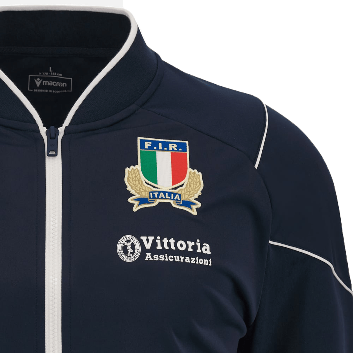 The Italy 6 Nations Full-Zip Anthem Jacket 23/24 by Macron is a navy blue jacket with white piping. It features the F.I.R. Italia logo on the right chest and the Vittoria Assicurazioni logo on the left chest, making it perfect for showing your support during the 6 Nations.