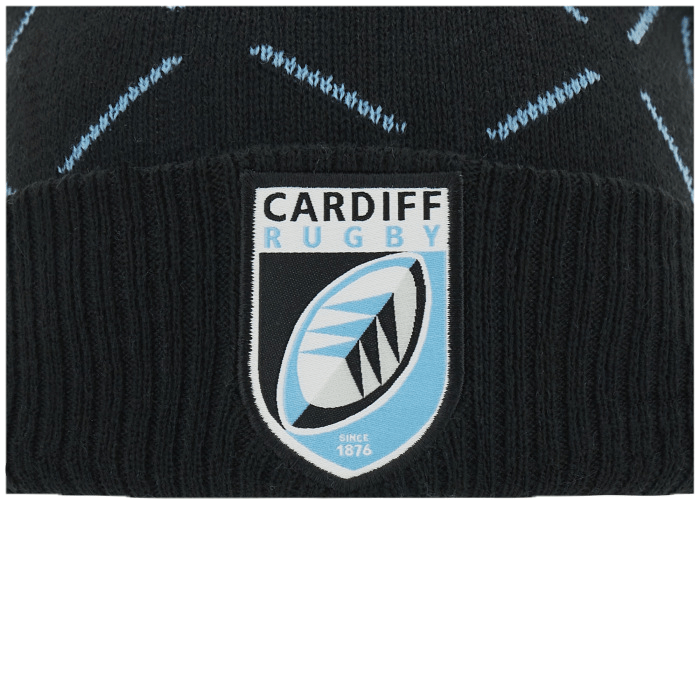 Close-up of a Cardiff Rugby logo on a black knit Cardiff Blues Pom Pom Beanie 23/24 by Macron with blue zigzag patterns.