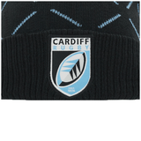 Close-up of a Cardiff Rugby logo on a black knit Cardiff Blues Pom Pom Beanie 23/24 by Macron with blue zigzag patterns.