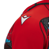 Close-up of a red athletic apparel jacket with a black and white Glasgow Warriors Training Jersey 23/24 by Macron logo on the shoulder.