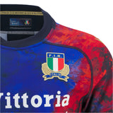 Close-up of the Italy 25/26 Replica Training Jersey by Macron, showcasing the F.I.R. Italia crest, sponsor logos, and a vibrant red and blue design.