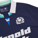 Close-up of the Scotland Authentic Home Jersey 24/25 by Macron, showcasing the team logo and a V-neck collar in white and teal. The word "Scotland" is clearly visible, with "Arnold" partially shown within the sponsor's logo. Celebrating 100 years of Murrayfield Stadium.