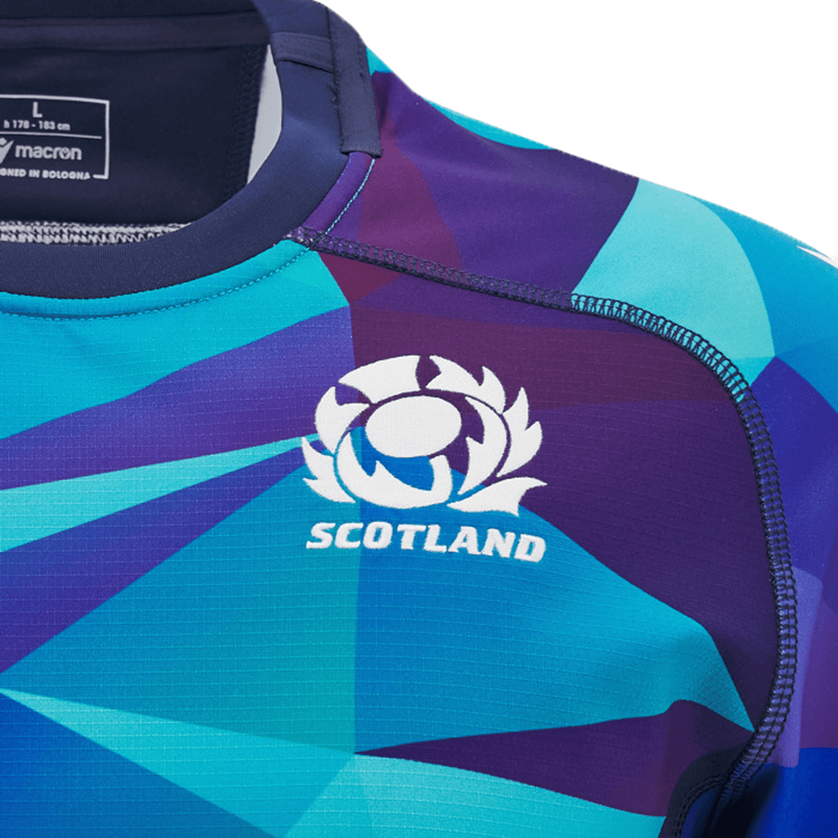 Close-up of a colorful Scotland Blue Training Jersey 24/25 by Macron, adorned with geometric patterns in blue and purple hues. The jersey features the word "SCOTLAND" and a thistle logo on the chest, while eco-mesh inserts enhance breathability in this design from Macron.