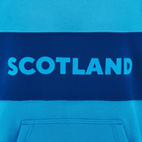 Close-up of the Scotland Block Leisure Hoodie 24/25 by Macron, featuring the word "Scotland" in bold, light blue letters on a darker blue horizontal stripe across the chest. A front pocket is visible at the bottom.