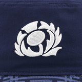 Close-up of a navy blue fabric featuring an embroidered white emblem of a stylized floral design, reminiscent of the 3D embroidered Scotland crest on the Scotland Bucket Hat 24/25 by Macron.