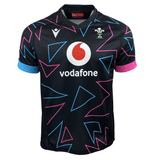 The Wales 24/25 Pathway Away Jersey by Macron showcases geometric blue and pink triangles, a Vodafone logo, and a dragon crest with "WRU" on the upper right. This stylish jersey exemplifies the timeless design of a classic Macron jersey.