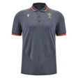 The Wales 24/25 Travel Polo by Macron is a dark gray soccer jersey adorned with subtle geometric patterns. It features red and yellow trim on the sleeves, a red collar edge, and an embroidered emblem on the chest, capturing the spirit of Wales for enthusiasts of both sport and travel.