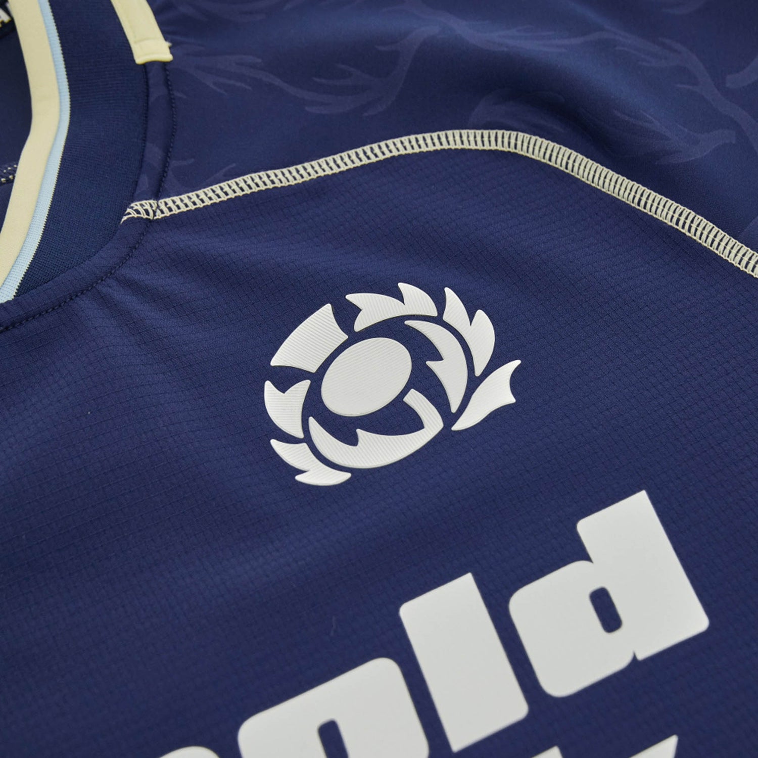 Close-up of the Scotland SRU 26/27 Authentic Matchday Home Jersey by Macron in navy blue, showcasing the white Scottish Rugby logo and part of a sponsor’s name in bold lettering—a genuine Macron authentic matchday shirt.