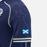 Sleeve detail from the Scotland SRU 26/27 Replica Home Jersey by Macron, featuring a navy sports jersey sleeve with a subtle antler pattern, cream trim, and a small blue and white Scottish flag patch on the lower sleeve—design elements inspired by the official Scotland rugby kit. This high-quality piece mirrors the craftsmanship of an authentic Macron Scotland jersey.