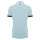 The Scotland SRU 26/27 Travel Polo by Macron is shown from the back in light blue, featuring a small Scottish flag beneath the collar and dark stripes on the sleeve cuffs.