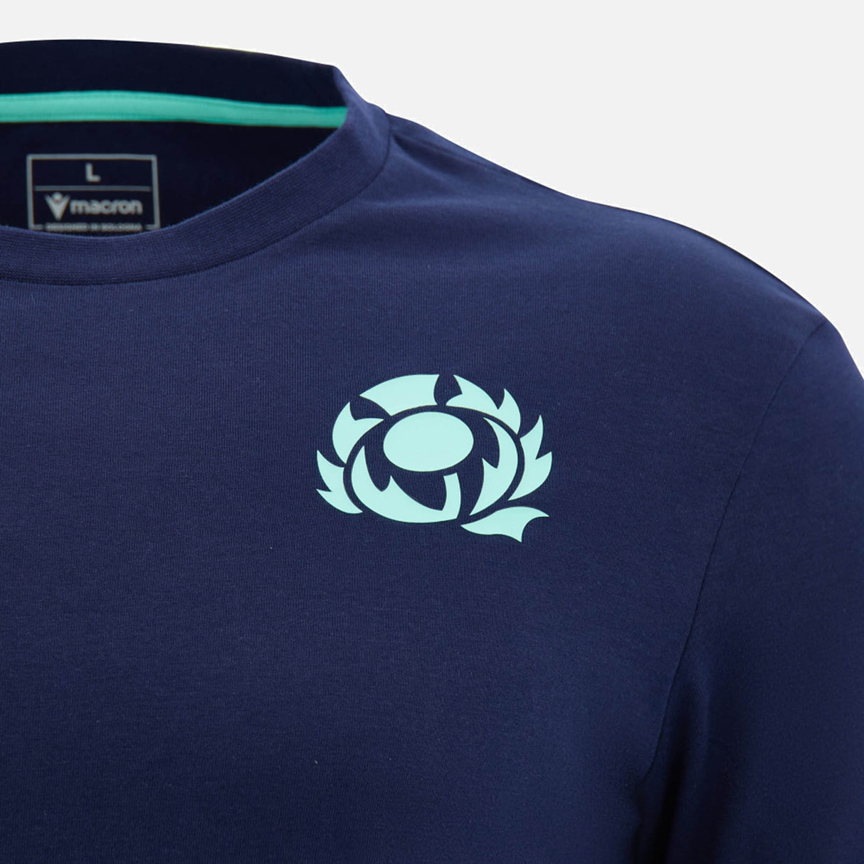 Close-up of the Scotland SRU 26/27 Leisure Cotton T-Shirt by Macron in navy blue, featuring a light blue thistle emblem on the chest and a "Macron" brand label inside the collar, inspired by the official Scottish Rugby Union kit.