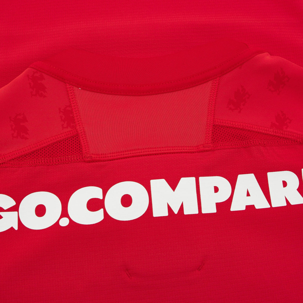 Close-up of the Wales WRU 26/27 Authentic Matchday Home Jersey by Macron in red, featuring part of the white “GO.COMPARE” sponsor text and subtle lion logos on the fabric near the collar—highlighting the premium details of this official Macron match jersey.