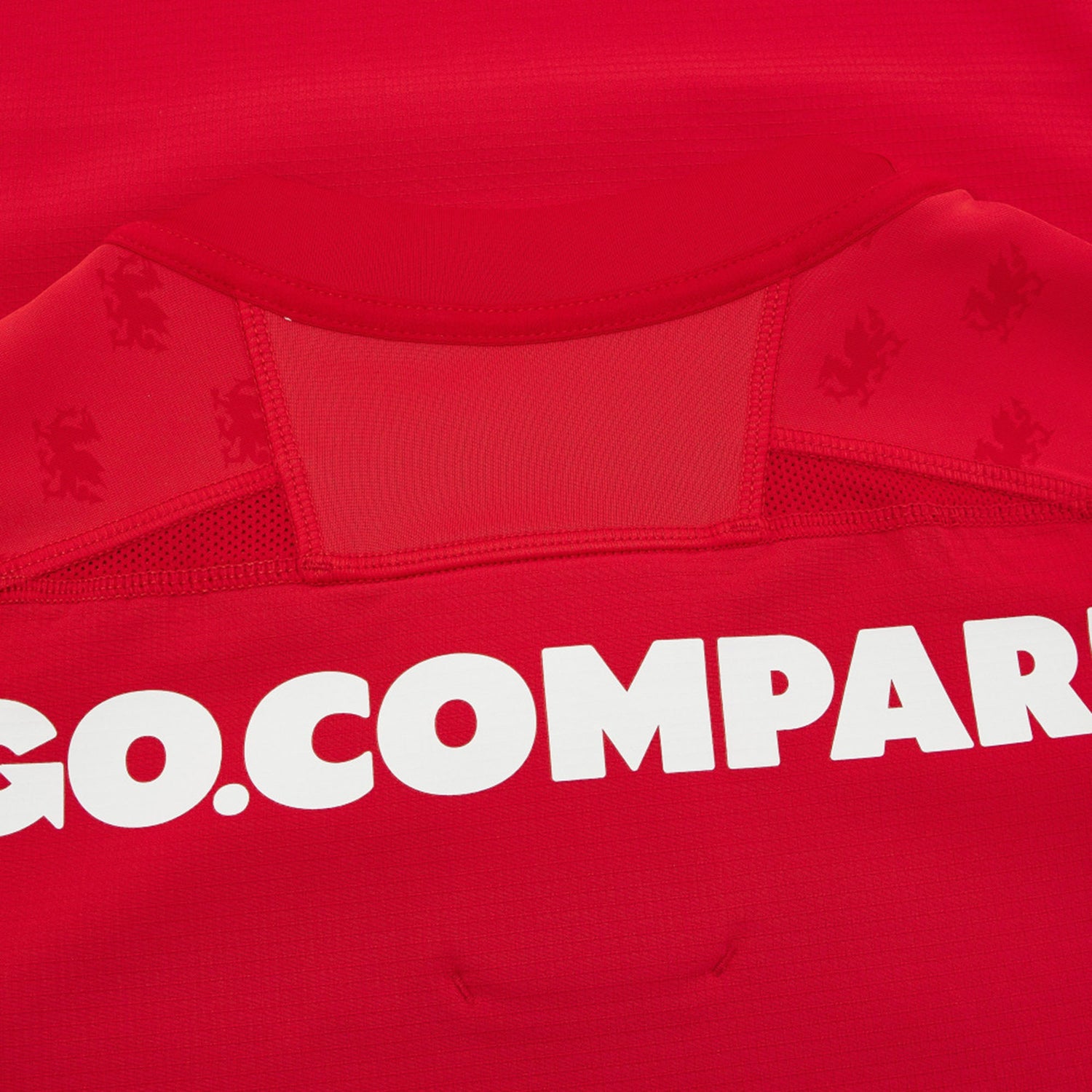 Close-up of the Wales WRU 26/27 Authentic Matchday Home Jersey by Macron in red, featuring part of the white “GO.COMPARE” sponsor text and subtle lion logos on the fabric near the collar—highlighting the premium details of this official Macron match jersey.