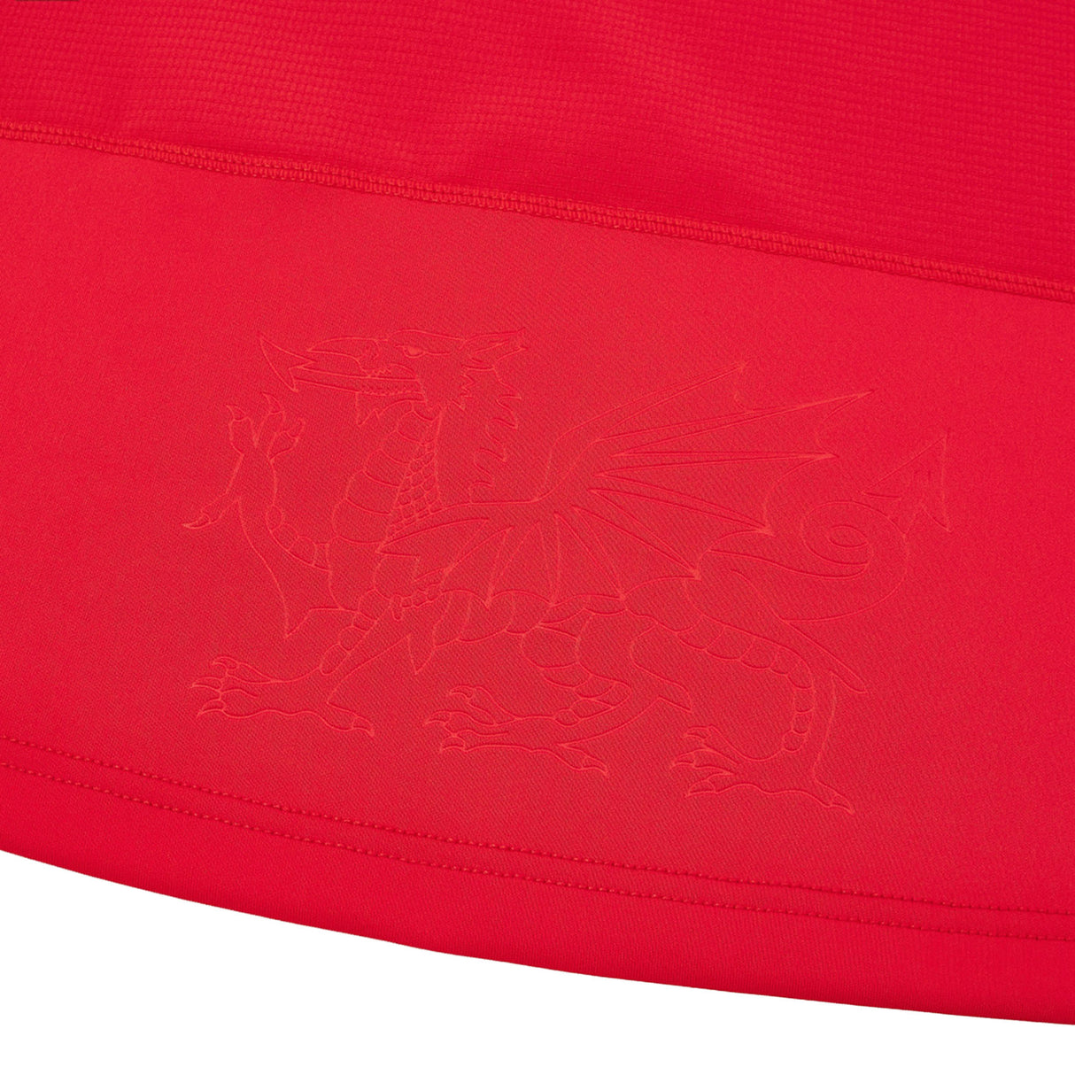 Scarlet fabric featuring an embossed dragon with outstretched wings and a pointed tail along the edge—just like that on the Wales WRU 26/27 Authentic Matchday Home Jersey by Macron.